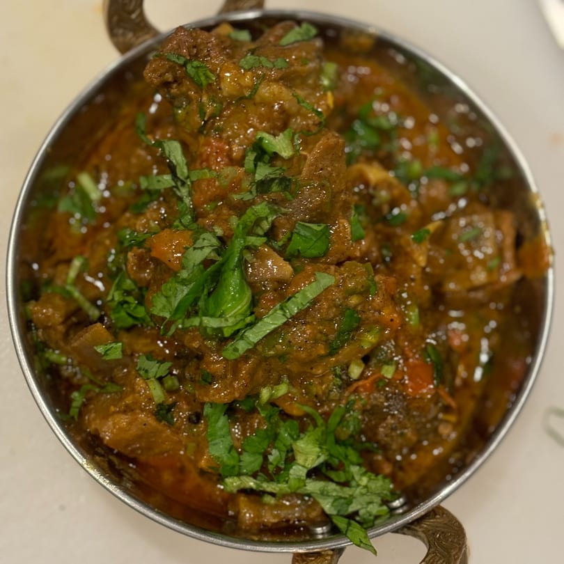 Close-up of a metal bowl filled with a rich, dark curry, garnished with fresh green herbs.