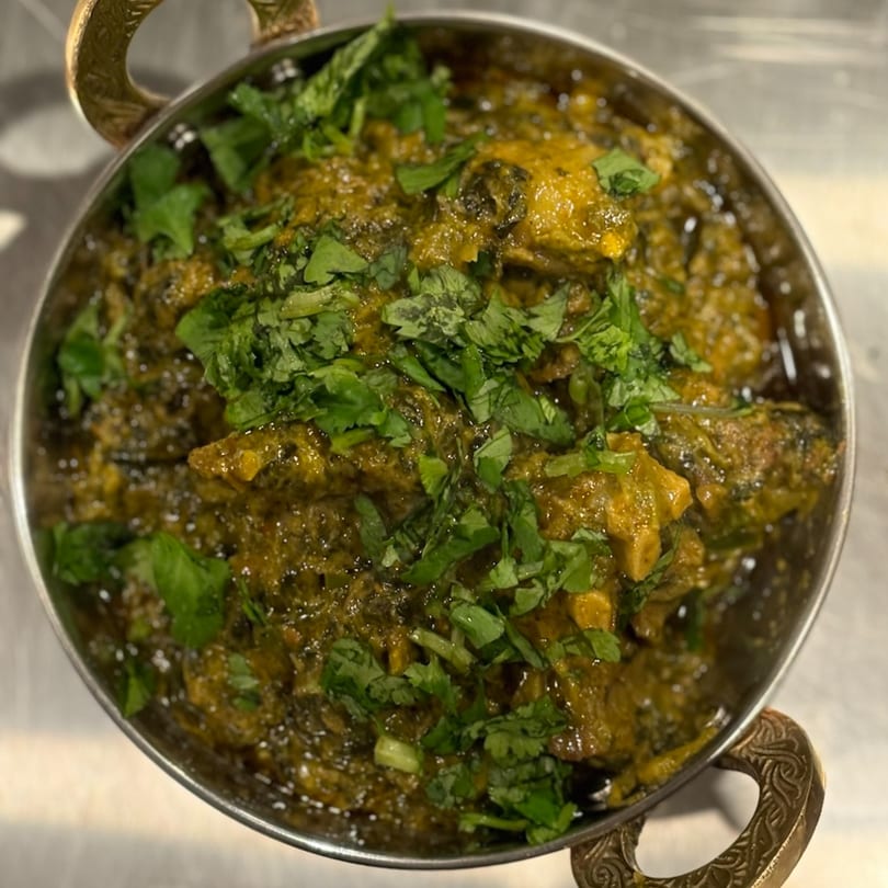 A close-up of a metal bowl filled with green curry, garnished with fresh cilantro.